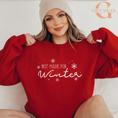 A woman wearing a red sweater with the text "NOT MADE FOR WINTER" printed on it, smiling and posing with her arms behind her back.