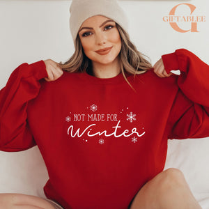 A woman wearing a red sweater with the text "NOT MADE FOR WINTER" printed on it, smiling and posing with her arms behind her back.
