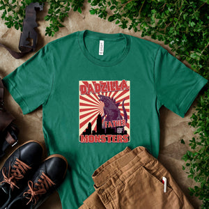 a green t-shirt with a graphic design of a Godzilla head and the text "DADZILLA FATHER OF MONSTERS" printed on it, along with a pair of brown pants and black shoes.