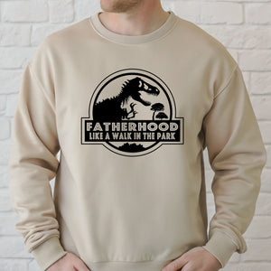 A man wearing a beige sweater with a graphic design featuring a dinosaur and the text "FATHERHOOD LIKE A WALK IN THE PARK".