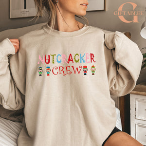 A woman wearing a beige sweater with the text "NUTCRACKER CREW" printed on it.