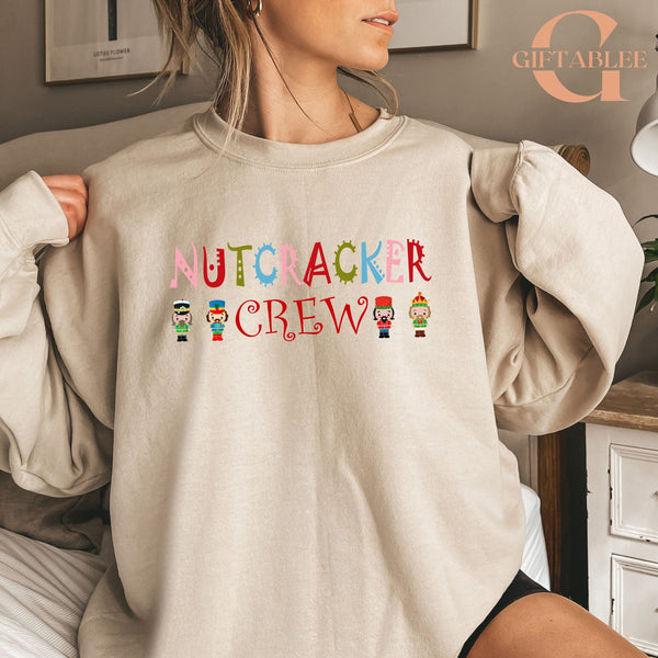 A woman wearing a beige sweater with the text "NUTCRACKER CREW" printed on it.
