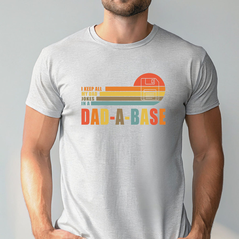 A man wearing a gray t-shirt with a graphic design that says "I keep all my dad jokes in a Dad-A-Base".