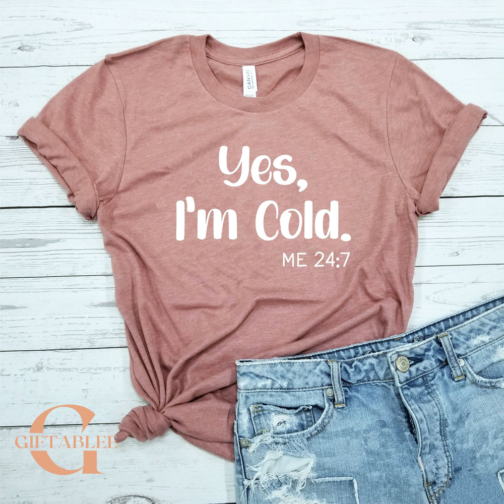 A pink t-shirt with the text "Yes, I'm Cold. ME 24:7" printed on it, along with a pair of blue jeans.