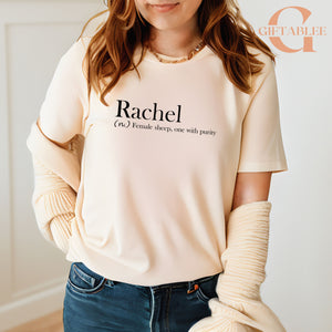 A woman wearing a white t-shirt with the word "Rachael" printed on it, standing in front of a white wall.