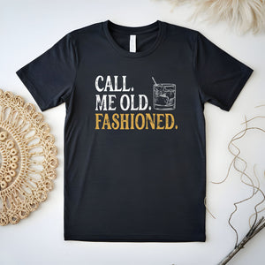 A black t-shirt with the text "CALL ME OLD, FASHIONED" printed on it, along with a graphic of a cocktail glass.