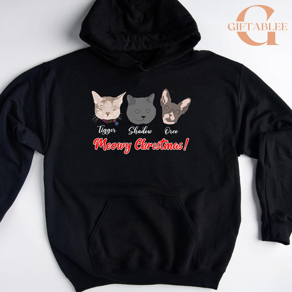 A black hoodie with a graphic design featuring three cat faces and the text "Meowy Christmas!"