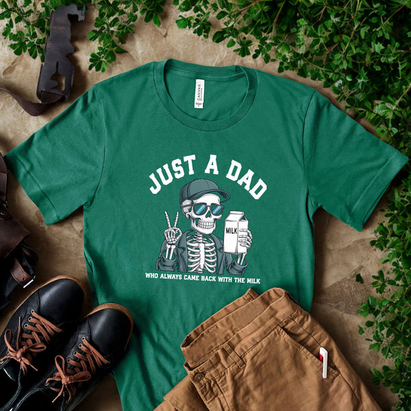 A green t-shirt with a skeleton wearing sunglasses and holding a carton of milk, accompanied by a pair of black shoes and a pair of khaki pants, all placed on a surface with greenery.