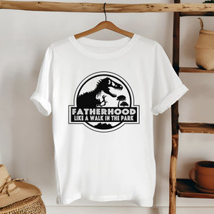 A white t-shirt with a graphic design featuring a dinosaur and the text "FATHERHOOD LIKE A WALK IN THE PARK".