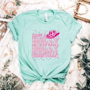 A turquoise t-shirt with a pink cowboy hat and the text "Have a Holly Dolly Christmas" printed on it, along with some greenery and beads.