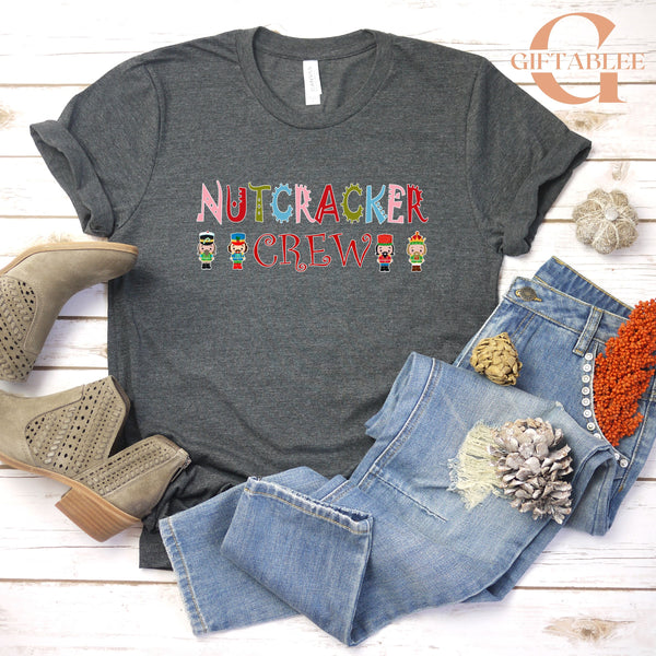 a casual outfit consisting of a gray t-shirt with a nutcracker crew design, a pair of jeans, and some accessories such as a pair of beige boots and a small flower.