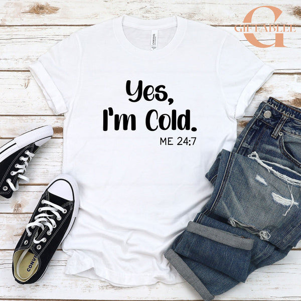 A white t-shirt with the text "Yes, I'm Cold. ME 24/7" printed on it, along with a pair of jeans and a pair of black and white sneakers.