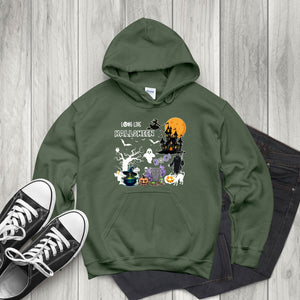 A green hoodie with a Halloween-themed graphic design, including a castle, ghost, pumpkin, and other spooky elements, is displayed on a wooden surface alongside a pair of black and white sneakers.