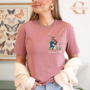 A woman wearing a pink t-shirt with a graphic of a couple and the text "Christmas 2016" is standing in front of a butterfly-themed wall art.