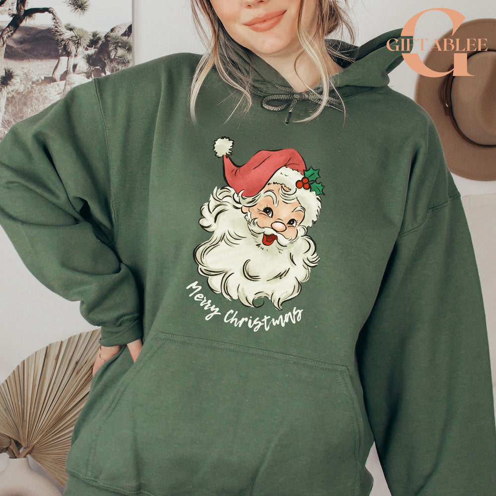 A woman wearing a green hoodie with a graphic of Santa Claus and the text "Merry Christmas" printed on it.