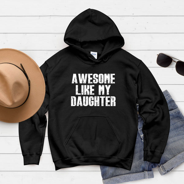 A black hoodie with the text "AWESOME LIKE MY DAUGHTER" printed on it, along with a pair of sunglasses and a hat, all laid out on a white background.