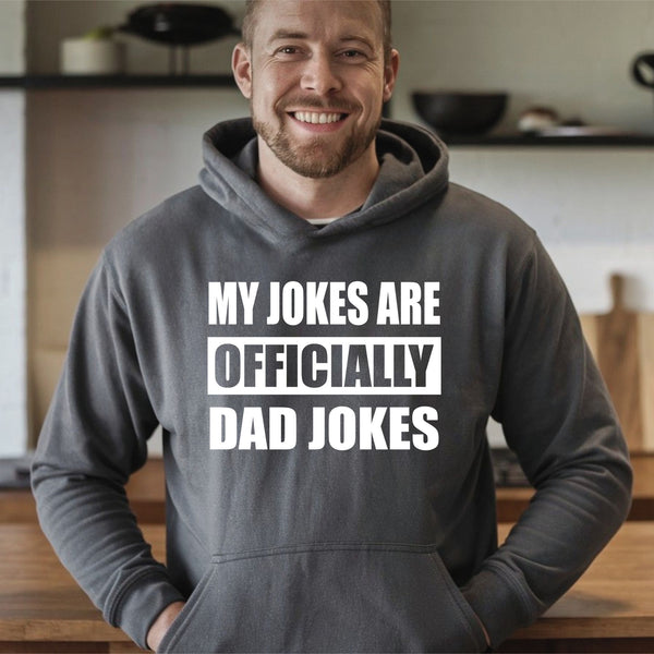 A man wearing a grey hoodie with the text "MY JOKES ARE OFFICIALLY DAD JOKES" printed on it, smiling at the camera.