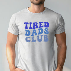 A man wearing a gray t-shirt with the text "TIRED DAD'S CLUB" printed on it.