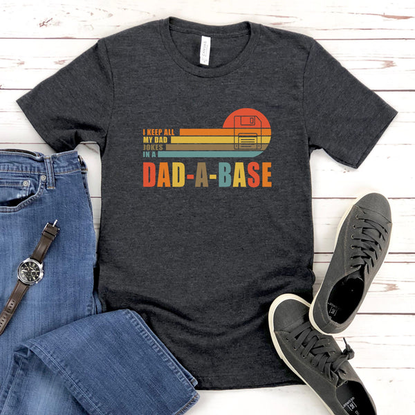 A gray t-shirt with a graphic design, a pair of jeans, and a pair of sneakers are laid out on a wooden surface.
