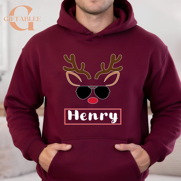 A man wearing a burgundy hoodie with a graphic of a reindeer wearing sunglasses and the name "HENRY" printed on it.