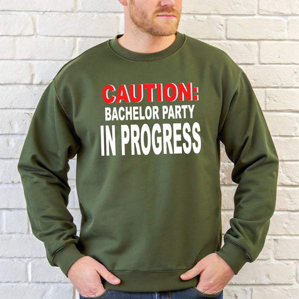 A man wearing a green sweatshirt with the text "CAUTION: BACCHELOR PARTY IN PROGRESS" printed on it.