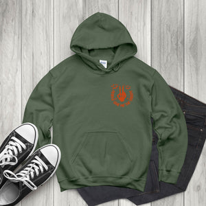 A green hoodie with an orange graphic design, a pair of black and white sneakers, and a pair of dark jeans are arranged on a wooden surface.