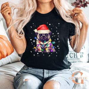 A woman wearing a black t-shirt with a graphic of a pug wearing a Santa hat and surrounded by Christmas lights.