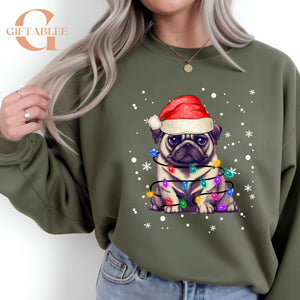 A woman wearing a green sweatshirt with a graphic of a pug dog wearing a Santa hat and surrounded by Christmas lights.