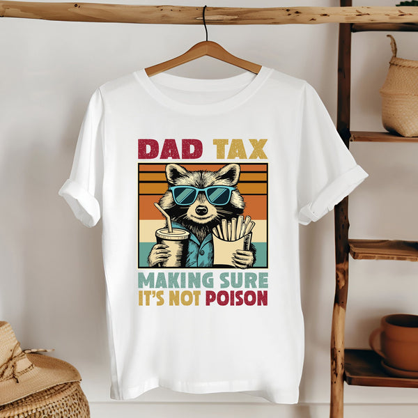 A white t-shirt with a graphic design featuring a raccoon wearing sunglasses and holding a cup of fries, along with the text "DAD TAX MAKING SURE IT'S NOT POISON".