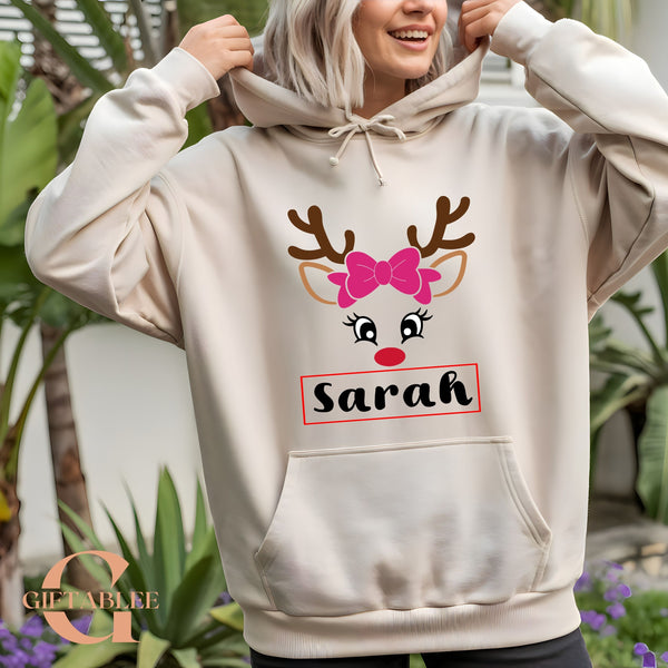 A woman wearing a white hoodie with a graphic of a deer's face and the name "Sarah" printed on it.