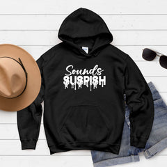 A black hoodie with the text "SOUNDS SUSPISH" printed on it, along with a pair of sunglasses and a hat, all laid out on a white background.