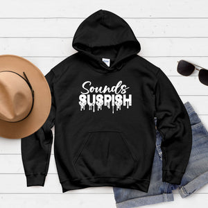 A black hoodie with the text "SOUNDS SUSPISH" printed on it, along with a pair of sunglasses and a hat, all laid out on a white background.