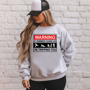 A woman wearing a gray sweatshirt with a graphic design on it, standing in front of a white brick wall.