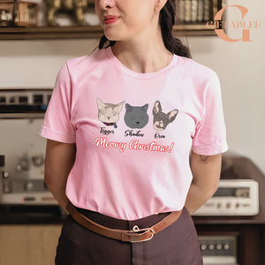 A woman wearing a pink t-shirt with a graphic design of three cat faces and the text "Meowy Christmas!" printed on it.