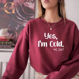 A woman wearing a maroon sweatshirt with the text "Yes, I'm Cold. ME 24:7" printed on it.