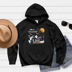A black hoodie with a Halloween-themed graphic design, including a ghost, jack-o-lantern, and other spooky elements, is displayed on a white background alongside a hat and sunglasses.