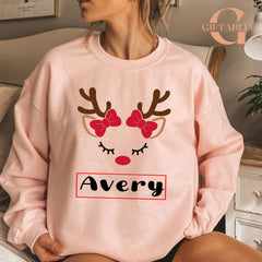 A woman wearing a pink sweatshirt with a reindeer face design and the name "Avery" printed on it.