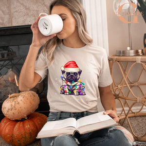 A woman is sitting on the floor, wearing a white t-shirt with a pug dog wearing a Santa hat and holding a book.
