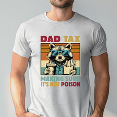 A man wearing a white t-shirt with a graphic design featuring a raccoon wearing sunglasses and holding a drink, along with the text "DAD TAX MAKING SURE IT'S NOT POISON".