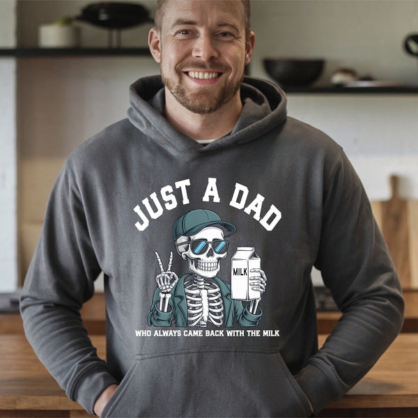 A man wearing a gray hoodie with a graphic design of a skeleton holding a carton of milk and the text "Just a Dad" smiling at the camera.