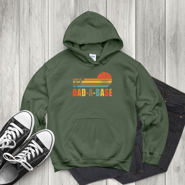 A green hoodie with a graphic design and text, along with a pair of black and white sneakers, are laid out on a wooden surface.