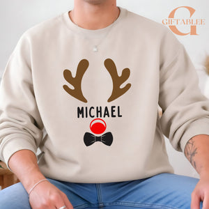 A person wearing a beige sweater with a graphic design featuring a pair of brown antlers and a red circle with a black bow tie.