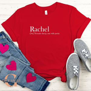 A red t-shirt with the word "Rachel" printed on it, along with a pair of jeans and gray sneakers, all laid out on a wooden surface.