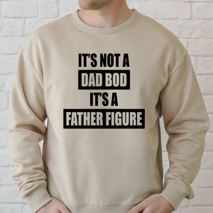 A man wearing a beige sweater with the text "IT'S NOT A DAD BOD IT'S A FATHER FIGURE" printed on it.