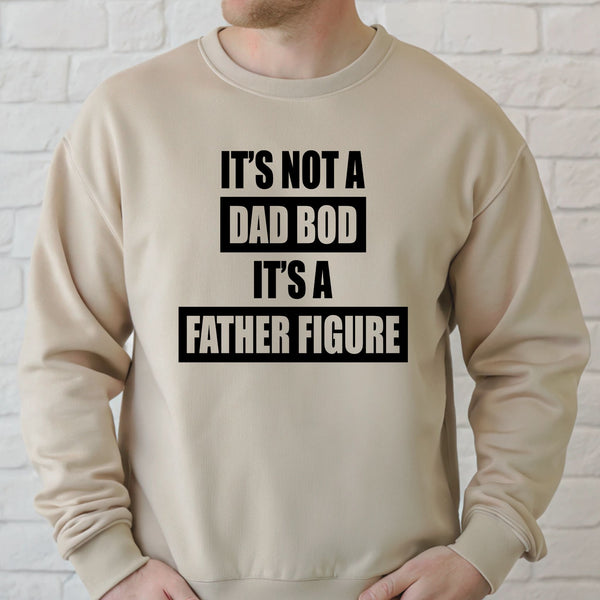 A man wearing a beige sweater with the text "IT'S NOT A DAD BOD IT'S A FATHER FIGURE" printed on it.