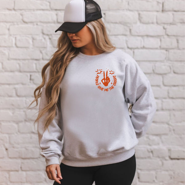 A woman wearing a gray sweatshirt with an orange graphic and a black baseball cap stands in front of a white brick wall.