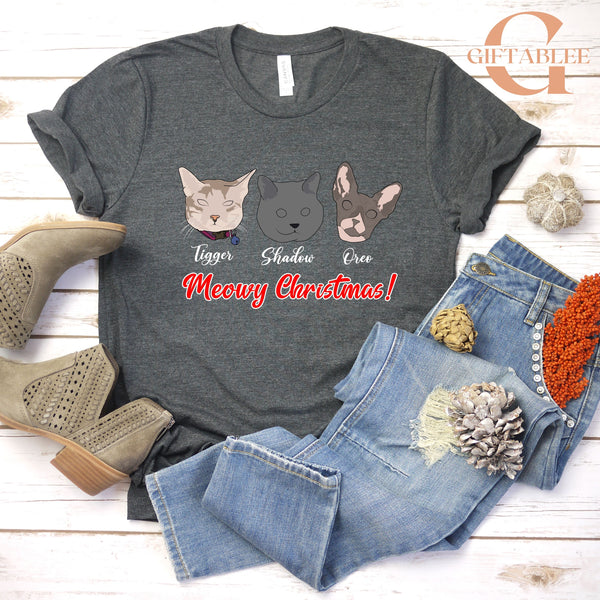 A gray t-shirt with a graphic design of three cat faces and the text "Meowy Christmas!" printed on it, along with a pair of jeans and boots.