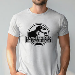 A man wearing a white t-shirt with a graphic design featuring a dinosaur and the text "FATHERHOOD LIKE A WALK IN THE PARK".