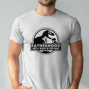 A man wearing a white t-shirt with a graphic design featuring a dinosaur and the text "FATHERHOOD LIKE A WALK IN THE PARK".