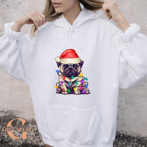 A woman wearing a white hoodie with a graphic of a pug dog wearing a Santa hat and surrounded by colorful Christmas lights.